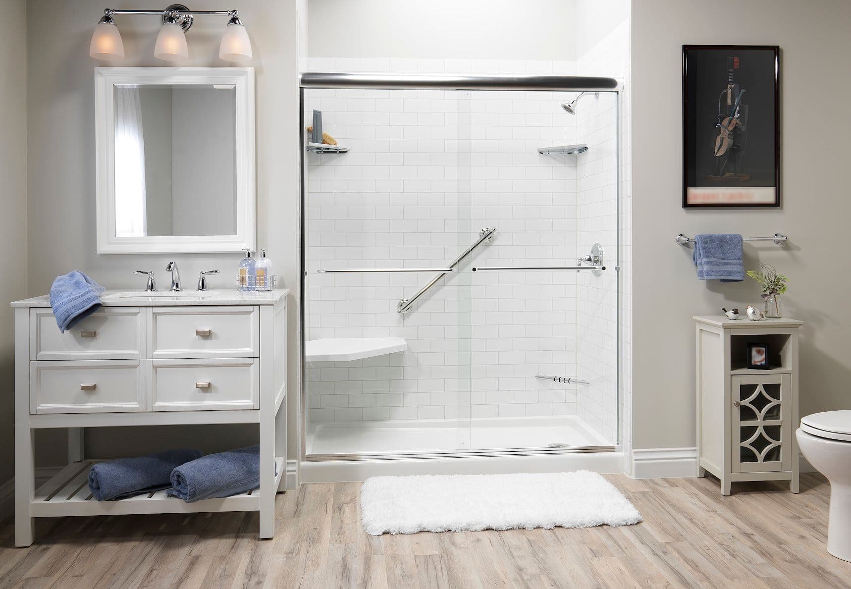 Stylish bathroom with a white vanity, a large mirror, and a glass-enclosed shower. Blue towels, wood floors, and soft lighting create a calm, inviting atmosphere.