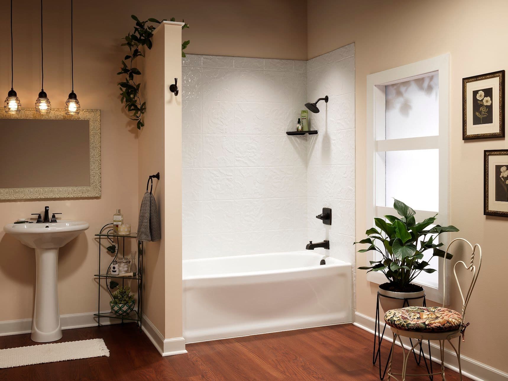 Modern bathroom with a white bathtub and pedestal sink. Warm lighting hangs above a mirror. Green plants and framed art add a cozy, elegant touch.