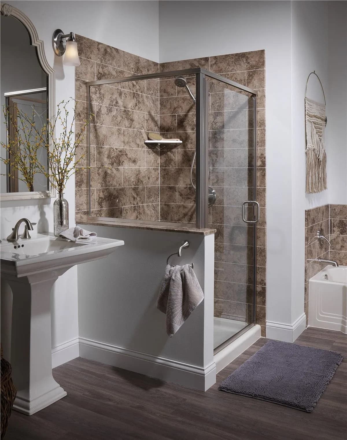Modern bathroom with a glass-walled shower featuring brown tiles. A pedestal sink with a silver faucet, a purple rug, and a towel add elegance.