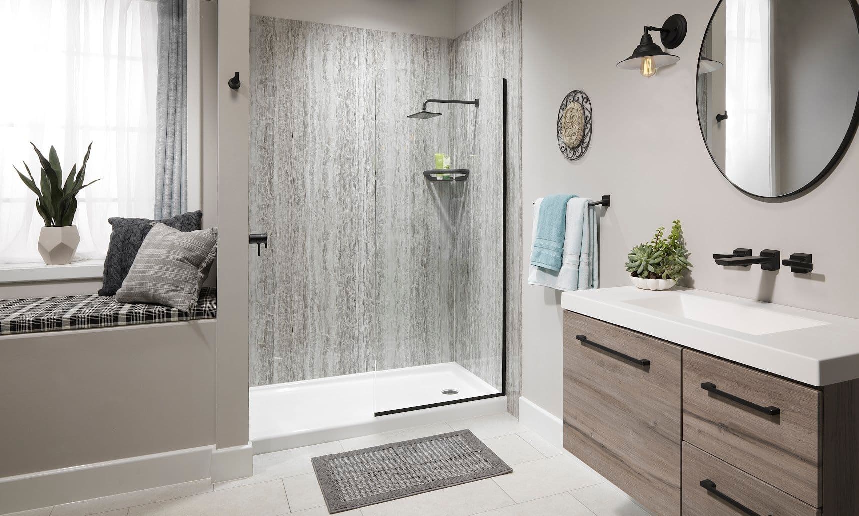 Modern bathroom with a sleek shower, wood vanity, and a round mirror. A window seat with cushions and plants adds a cozy touch. Soft lighting enhances the neutral palette.