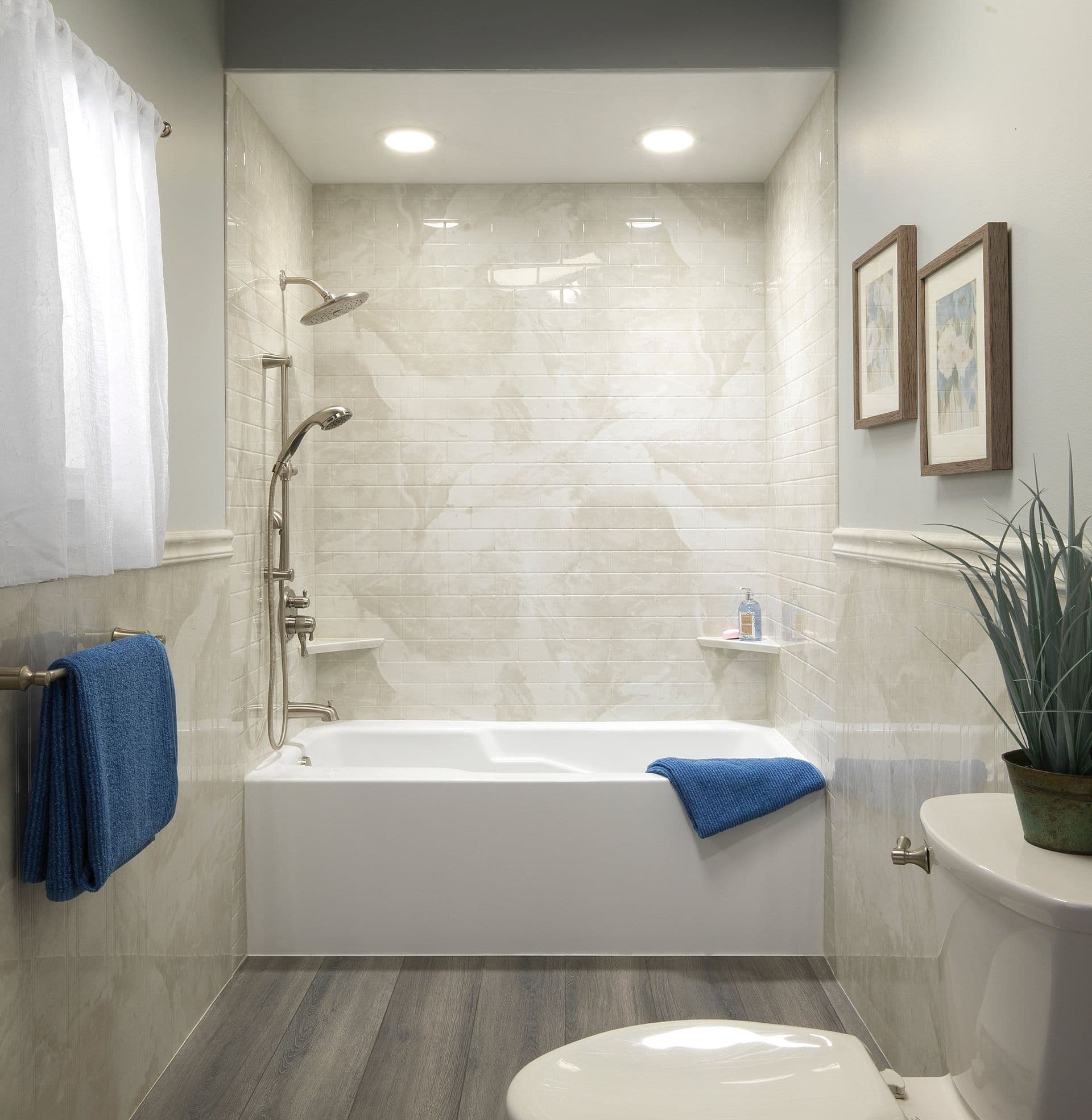 White rectangular bathtub against marble-tiled walls with gold fixtures, set on light wood flooring. The space is clean and minimalist.