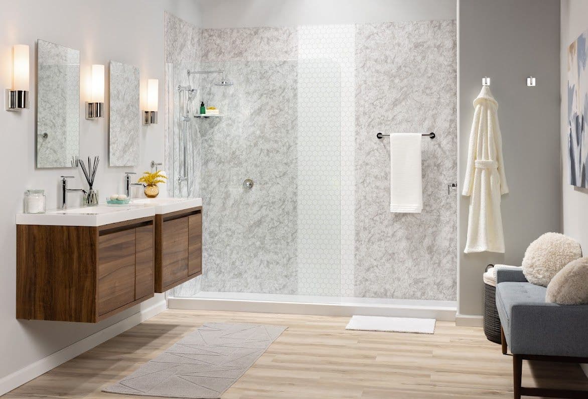 Modern bathroom with grey marble shower, wooden vanity with dual sinks, and decorative lighting. Minimalist decor includes neutral tones and a robe.