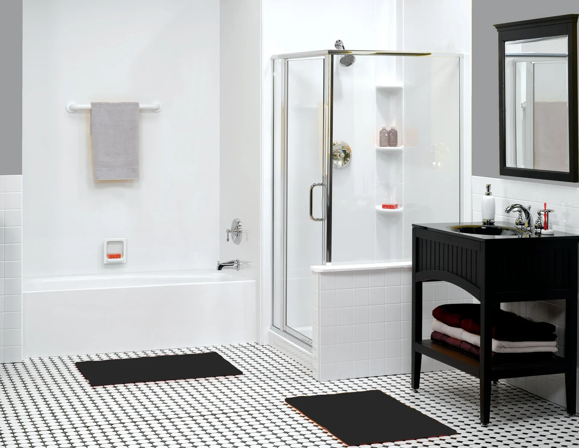 Modern bathroom with a white bathtub and a separate glass shower. The floor features black-and-white tiles, with two black mats. A sleek black vanity holds towels, and a mirror is mounted above. The atmosphere is clean and minimalist.