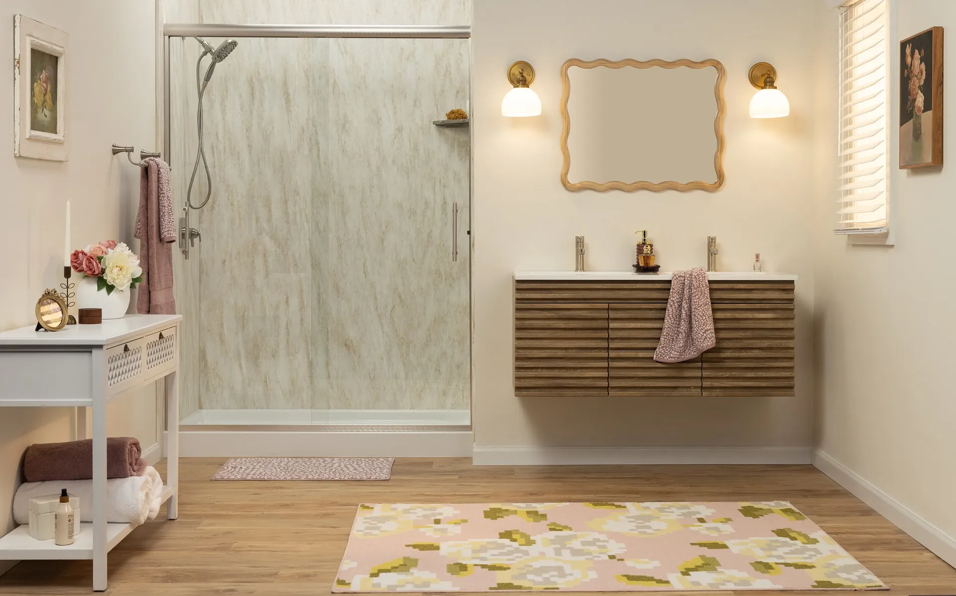 Modern bathroom with a glass shower, wooden vanity, and dual sinks. Warm tones, floral rug, soft lighting, and elegant décor create a cozy atmosphere.